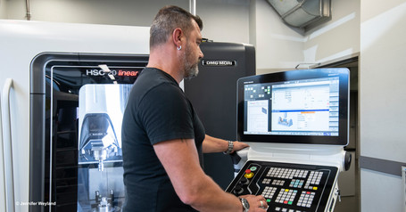 Ein Mann steht an einer CNC-Fräse und schaut auf die digitale Steuerung