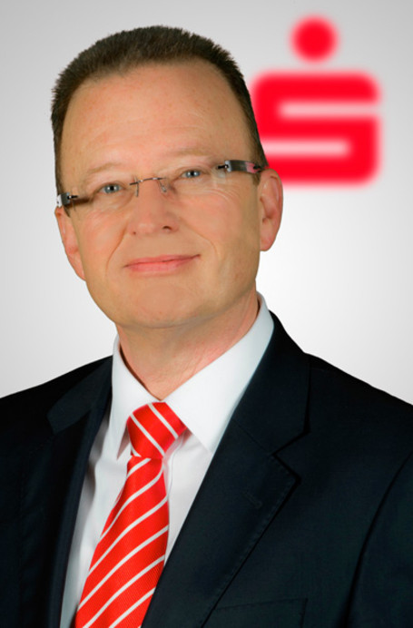 Ein Mann mit Krawatte und Brille vor einem Sparkassen-Logo